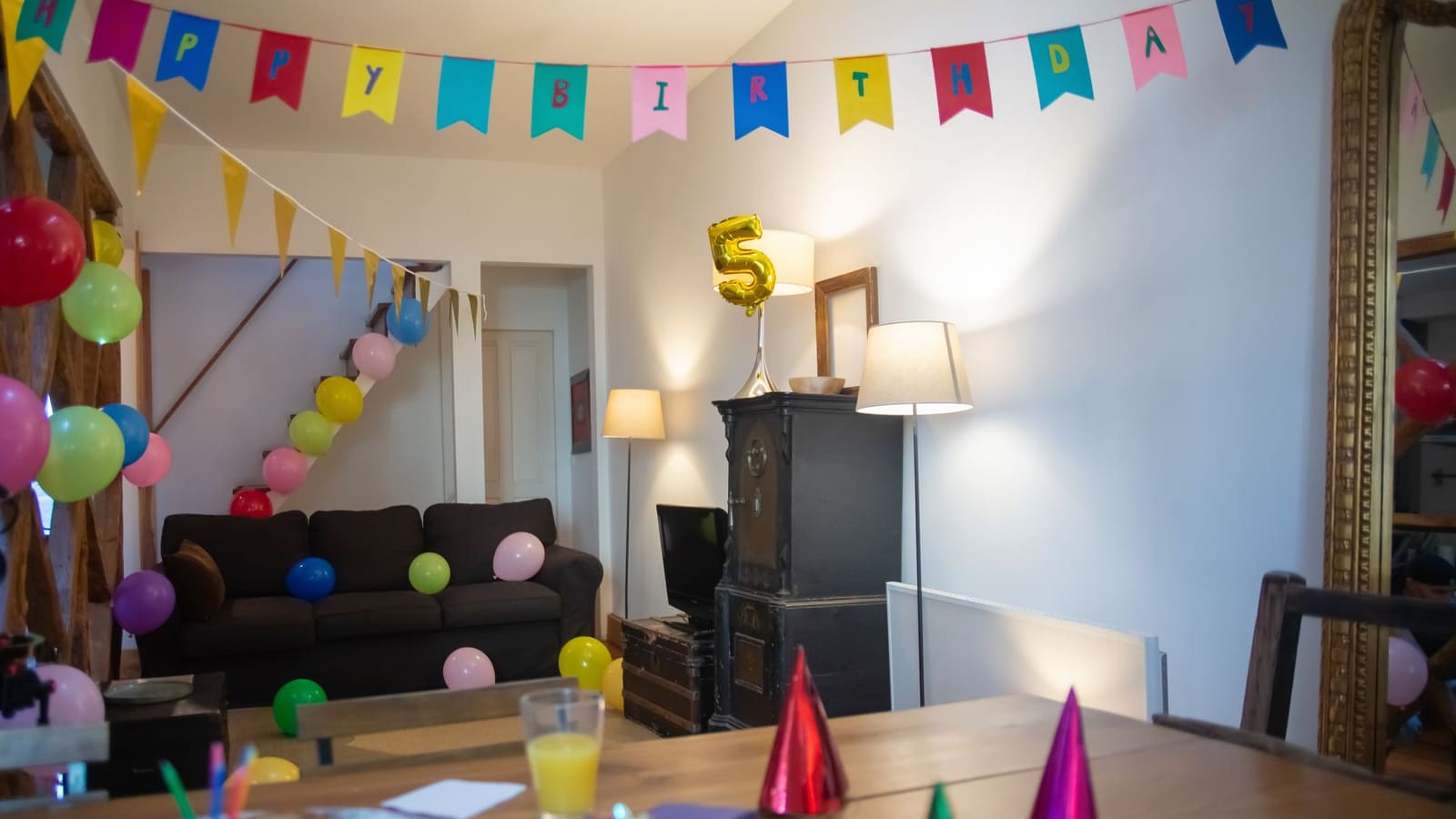 A living room decorated for a birthday with Happy Birthday bunting, balloons on the wall and cupcakes on the table
